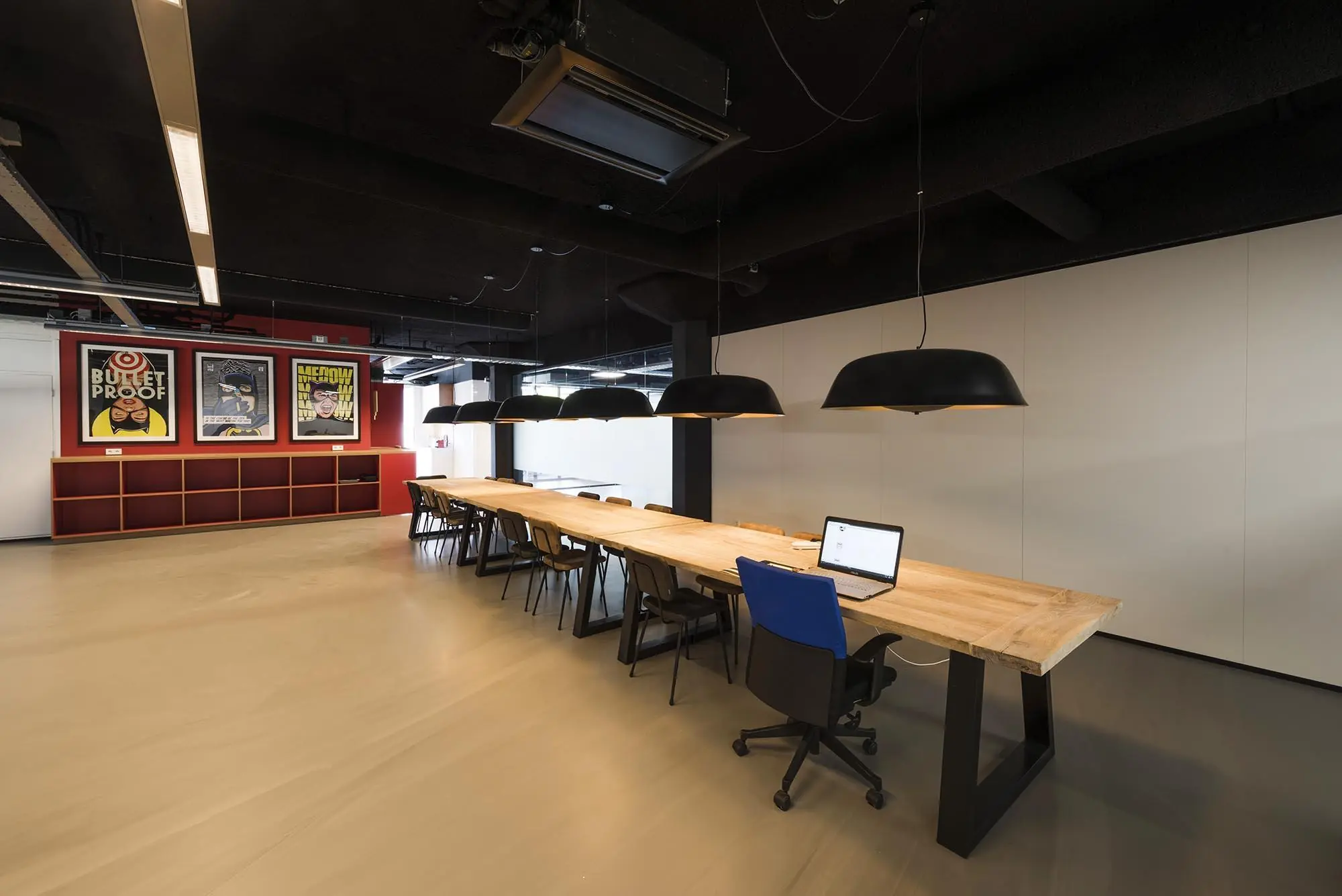 Moderne kantoorruimte aan de Anthony Fokkerweg met een lange houten vergadertafel, hanglampen en kleurrijke posters aan de muur.